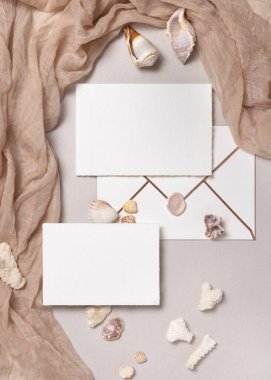 Boş kağıt kağıtların ve bej taşın üzerinde deniz kabukları, mercan ve bej kumaşlı zarfların bir kopyası. Plaj partisi deniz kırtasiyesi davetiyeler ve yaz partisi kartları için.