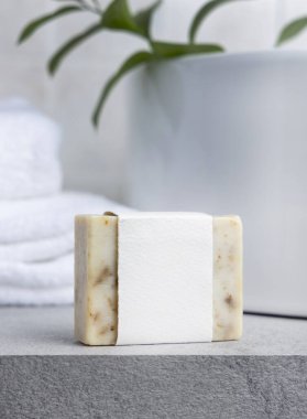 Yeşil yapraklı, beyaz banyo havluları ve gri taş tezgahın üzerinde boş etiketli krem sabun kalıbı kapatılıyor, ambalaj modeli yapılıyor. Doğal el yapımı bitkisel hijyen ürünü. Tarafsız tuvalet