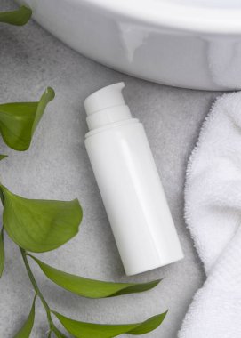 Paket maketi, beyaz boş bir pompa krem şişesi yeşil yapraklı dal, leğen ve beyaz banyo havlularıyla banyo manzaralı gri taş tezgahta. Doğal bitkisel kozmetik