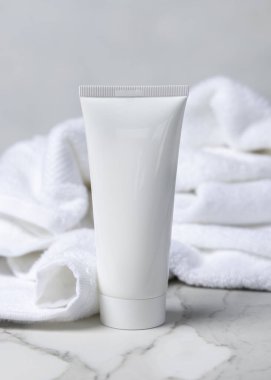 Banyoda beyaz banyo terry havlusunun yanında beyaz sıkılmış kozmetik tüpün bir kopyası. Etiket alanı boş. Kopyalama alanı olan nötr arkaplan. Spa otel içeriği. Vücut ya da yüz kremi paketleme