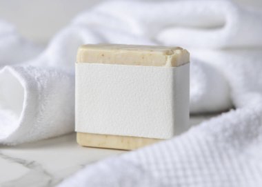 Beyaz banyo havlularının yanında boş kağıt etiketli bej, katı sabun kalıbının bir kopyası. Dikdörtgen şeklinde. Tarafsız arkaplanda fotokopi alanı olan markasız ambalaj. Kişisel bakım paketleme