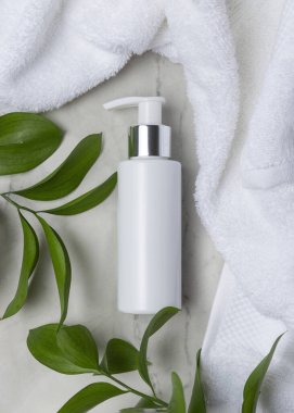 Beyaz Terry havlusunun yanında boş beyaz pompa şişesi ve taşın üstünde yeşil yapraklar, üst manzara. Gümüş yakalı ve fotokopi alanlı markasız kozmetik ambalajlar. Cilt ürünleri