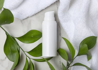 Beyaz Terry havlusunun yanında boş beyaz pompa şişesi ve taşın üstünde yeşil yapraklar, üst manzara. Kopya alanı ile markasız kozmetik paketleme. Cilt ürünüyle tarafsız banyo sahnesi