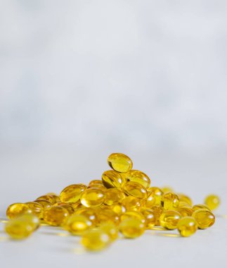 Pile of small yellow softgel on greige stone with copy space, close up. Nutritional supplements or vitamins for health and wellness, Omega 3 fish oil capsules