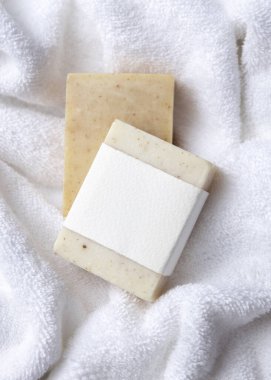 Açık bej, katı sabun kalıbının bir kopyası. Beyaz banyo terli havlularının üzerinde boş etiket var. Tarafsız arkaplanda, fotokopi alanı ile markasız paketleme, üst görünüm. Kişisel bakım bağlamı