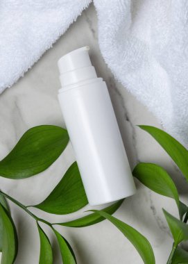 Beyaz Terry havlusunun yanında boş beyaz pompa şişesi ve taşın üstünde yeşil yapraklar, üst manzara. Kopya alanı ile markasız kozmetik paketleme. Cilt ürünüyle tarafsız banyo sahnesi