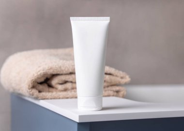 Banyodaki bej banyo havlusunun yanında beyaz, boş plastik kozmetik tüp maketi. Kapatın, kopyalayın. Krem, losyon ya da jel ambalajlama. Cilt ürünleri