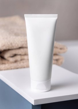 Banyodaki bej banyo havlusunun yanında beyaz, boş plastik kozmetik tüp maketi. Kapatın, kopyalayın. Krem, losyon ya da jel ambalajlama. Cilt ürünleri