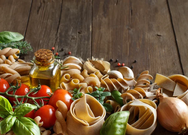 Whole wheat pasta, vegetables,  herbs and olive oil on wooden ba — Stock Photo, Image