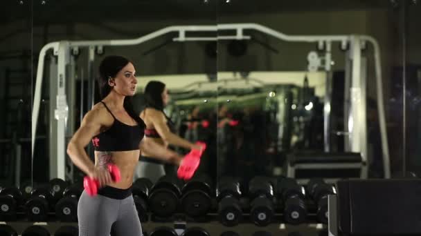 Chica de fitness posando en el banco en el gimnasio. levanta la mancuerna — Vídeos de Stock