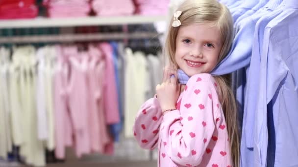 Девочка смотрит на одежду в модном магазине — стоковое видео