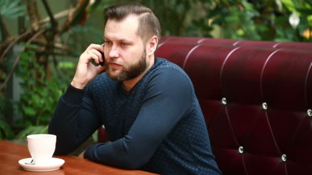 Handsome bearded businessman talking on the phone cheerfully during his coffee break on the cafe terrace — Stock Video