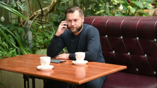Geschäftsmann sitzt im Café und telefoniert und trinkt Kaffee. Beschäftigter Mann im Café im Gespräch mit Freunden. — Stockvideo
