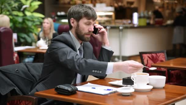 Красивый бородатый бизнесмен весело разговаривает по телефону во время кофе-брейка на террасе кафе — стоковое видео