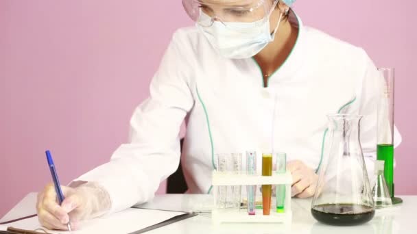 Химик-женщина сравнивает пробирки с химикатами. защитные очки — стоковое видео