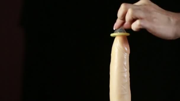 Руки женщины, показывающей использование презерватива на пластиковой модели пениса — стоковое видео