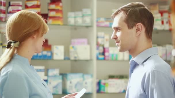Mujer Farmacéutica ofrece al visitante una cura en la farmacia — Vídeo de stock