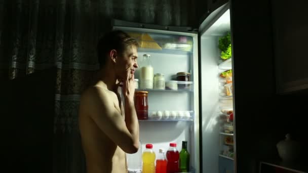 El hombre de la noche se para en el refrigerador abierto. comiendo sándwich. chico hambriento — Vídeos de Stock