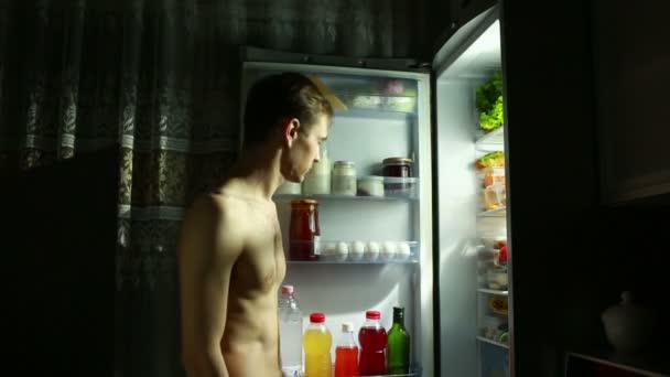 El hombre de la noche se para en el refrigerador abierto. comiendo sándwich. chico hambriento — Vídeo de stock