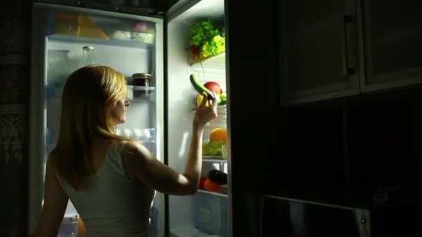 Сексуальная женщина открывает холодильник ночью. выбирает огурец — стоковое видео