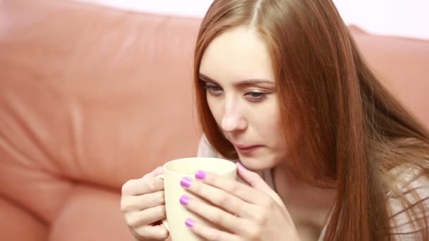 Portrait of oung beautiful woman with a cup on sofa — Stock Video