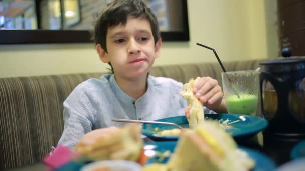 Gyermekeim, fiú eszik szendvicseket a kávézóban. hasábburgonyával — Stock videók