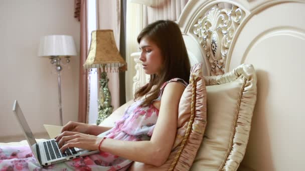 Молодая девушка, работающая за компьютером в постели. социальные сети — стоковое видео