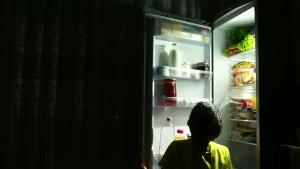 Child eating a snack in front of the refrigerator in the middle of the night. — Stock Video