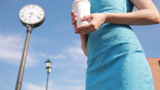 Chica se para cerca del reloj y beber café. esperando — Vídeo de stock