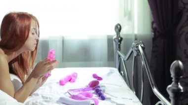 Young woman holding dildo on bed. Girl chooses a vibrator. lot of sex toys