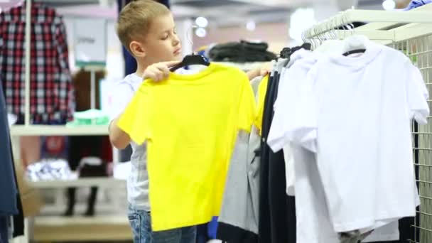 Schattige lachende jongen staat in de buurt van kleding en kiezen — Stockvideo