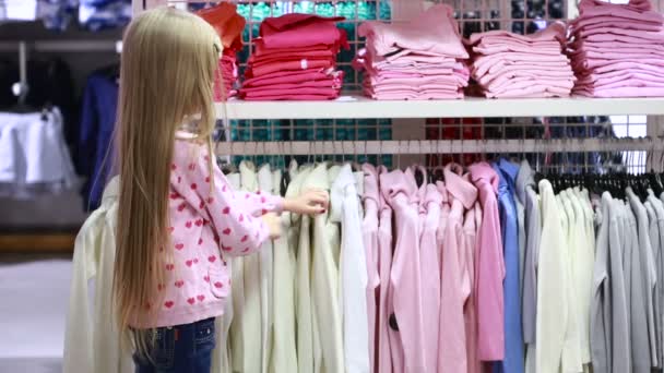 Negozio alla moda. Una ragazzina in un negozio di abbigliamento. sceglie un abito — Video Stock