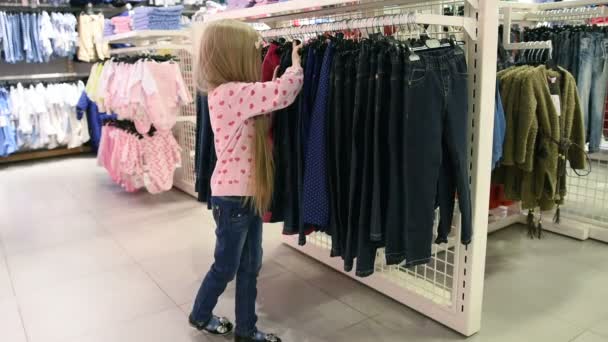 Tienda de moda. Una niña en una tienda de ropa. elige un traje — Vídeos de Stock