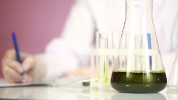 Química femenina comparando tubos de ensayo con productos químicos. gafas protectoras — Vídeo de stock