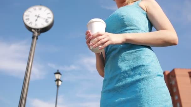 Κορίτσι στέκεται κοντά στο ρολόι και πίνοντας καφέ. αναμονής — Αρχείο Βίντεο