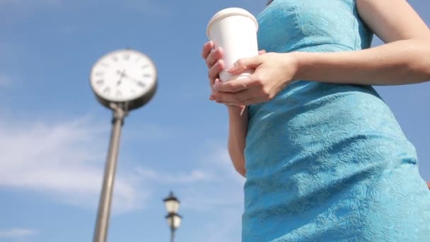 ผู้หญิงยืนอยู่ใกล้กับนาฬิกาและดื่มกาแฟ รอ — วีดีโอสต็อก