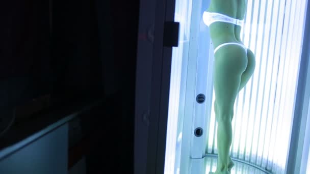 Hermosa chica se para en el solarium y tomar el sol en los rayos — Vídeo de stock