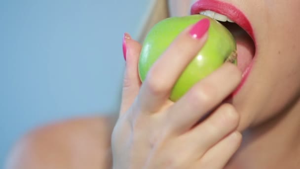 Mooi meisje eet een groene appel op een blauw — Stockvideo