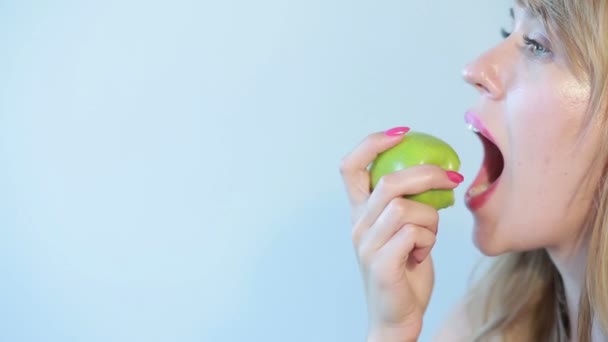 Schönes Mädchen isst einen grünen Apfel auf einem blauen — Stockvideo