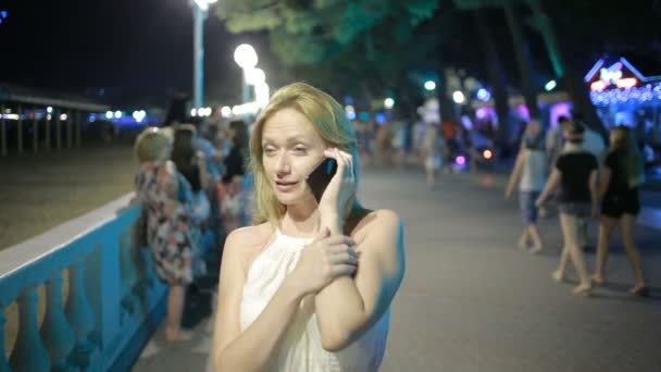 Симпатичная женщина со смартфоном стоит на набережной по ночам — стоковое видео