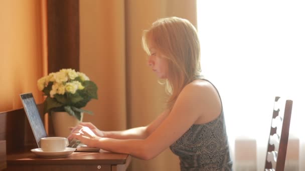 Mooie vrouw bezig met een laptop die zittend op de tafel in het huis. — Stockvideo