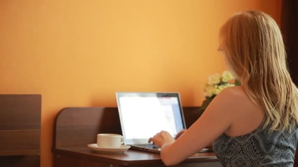 Beautiful woman working on a laptop sitting on the table in the house. — Stock Video