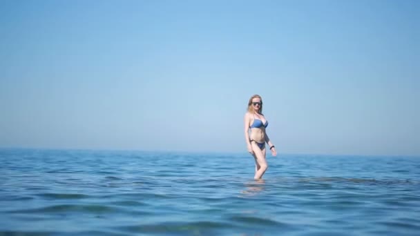 Sexy dívka v modrých bikinách baví stojí ve vodě. na pláži ve vlnách — Stock video