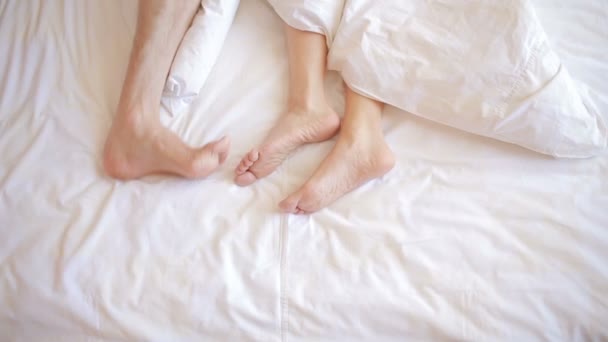 Un hombre y una mujer en la cama. piernas masculinas y femeninas vista superior, ropa de cama blanca — Vídeos de Stock