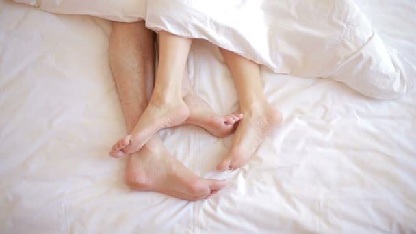 Ένας άνδρας και μια γυναίκα στο κρεβάτι. Ανδρική και γυναικεία πόδια κάτοψη, λευκά είδη — Αρχείο Βίντεο