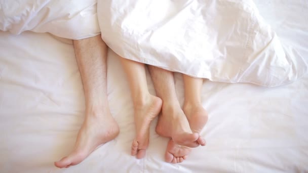 Un hombre y una mujer en la cama. piernas masculinas y femeninas vista superior, ropa de cama blanca — Vídeo de stock
