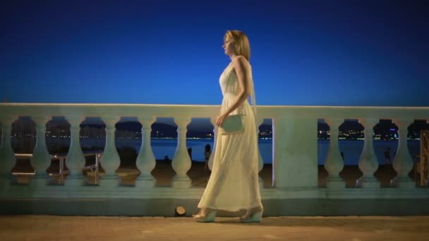 Κορίτσι σε ένα μακρύ λευκό φόρεμα. περιπάτους κατά μήκος της παραλίας το βράδυ. — Αρχείο Βίντεο