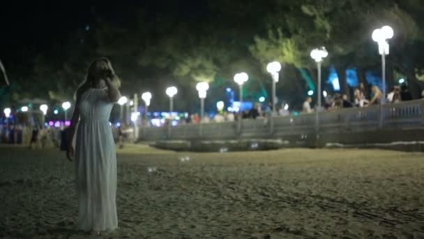 Meisje op het strand te lopen. het drinken van wijn. Nacht resort. vrouw in witte jurk — Stockvideo