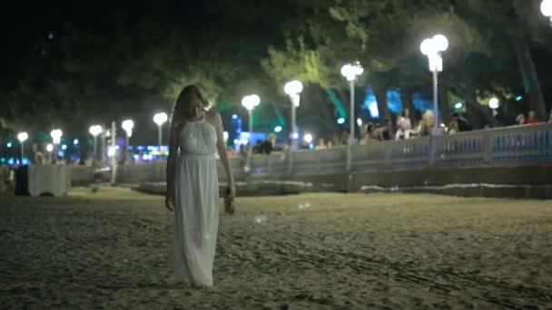 Дівчина гуляє на пляжі. пити вино. Нічний курорт. жінка в білій сукні — стокове відео