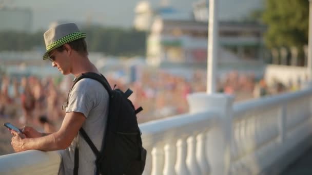 Молодой счастливый человек пользуется смартфоном у моря. туристические прогулки вдоль набережной — стоковое видео